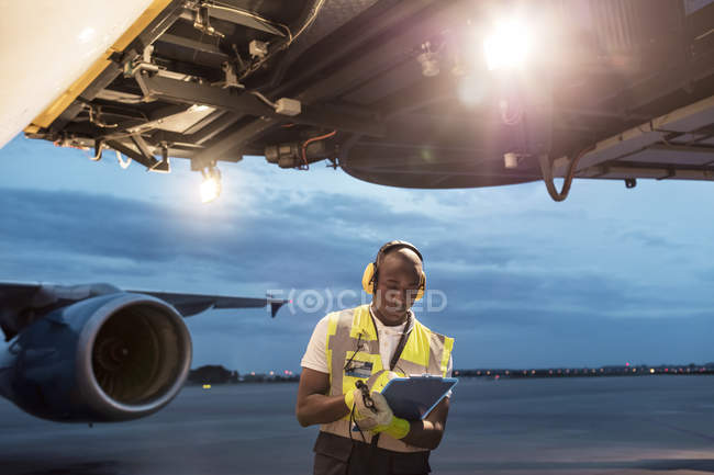 Airport ground crew worker with clipboard under airplane on tarmac — Stock Photo