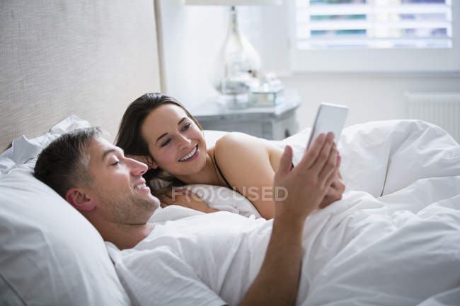 Pareja sonriente acostada en la cama usando tableta digital - foto de stock