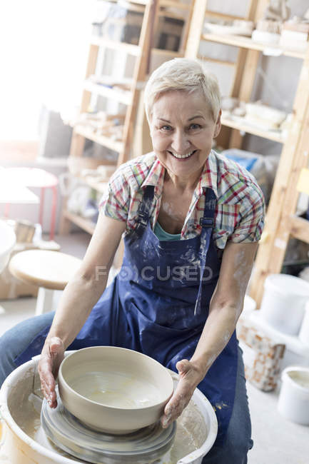 Retrato sonriente mujer mayor usando rueda de cerámica en el estudio - foto de stock