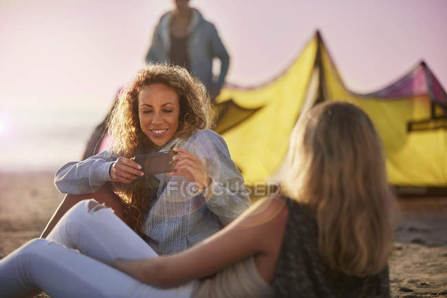 Las mujeres usando el teléfono de la cámara en la playa - foto de stock