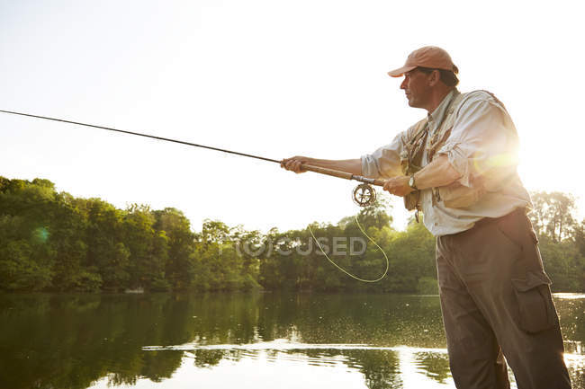 Старший чоловік літає на риболовлю на літньому озері — стокове фото