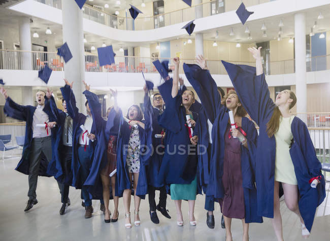 Выпускники колледжа в шапке и халате бросают шапки над головой — стоковое фото