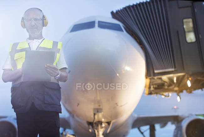 Controlador de tráfico aéreo retrato con portapapeles delante del avión en asfalto del aeropuerto - foto de stock