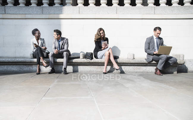 Corporate business people working on sunny bench outdoors — Stock Photo