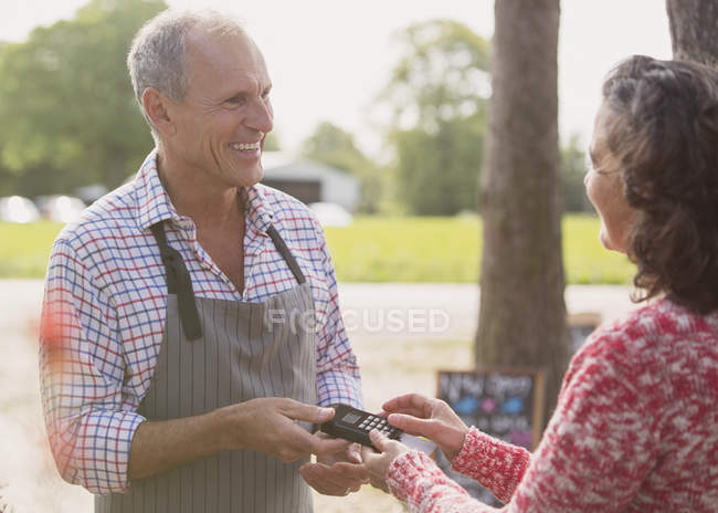Trabajador de vivero de planta sonriente que ofrece máquina de tarjeta de crédito al cliente - foto de stock