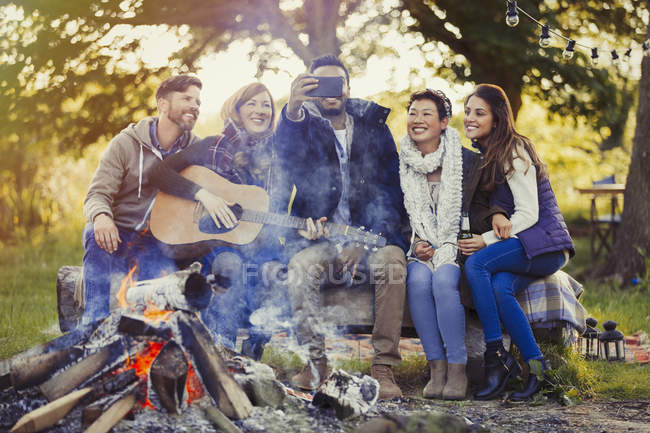 Smiling friends with camera phone taking selfie at campfire — Stock Photo