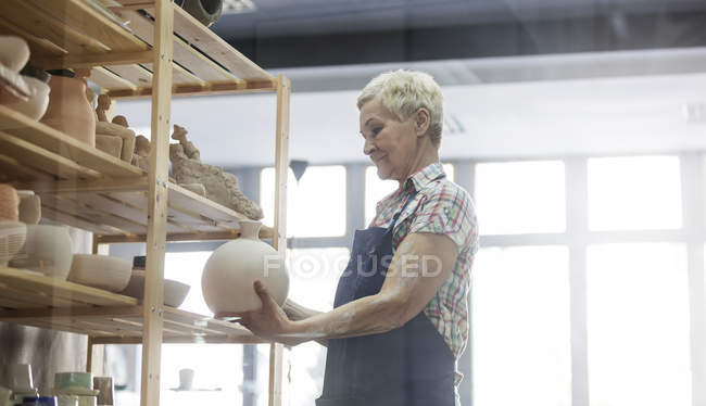 Mujer mayor colocando jarrón de cerámica en el estante en el estudio - foto de stock
