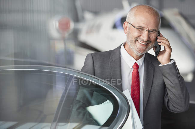 Un hombre de negocios sonriente hablando por teléfono celular en el hangar del avión - foto de stock