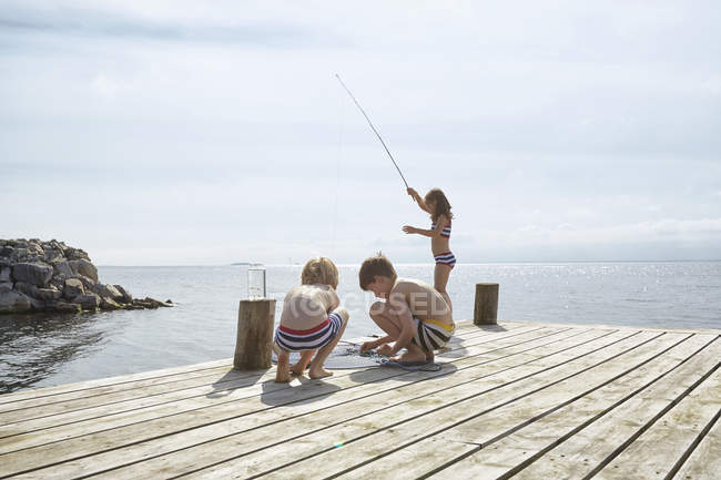 Хлопчики і дівчинка рибалять біля сонячного причалу на березі озера — стокове фото