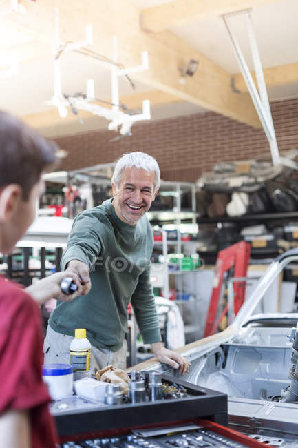 Усміхнений батько бере інструмент від сина в авторемонтному магазині — стокове фото