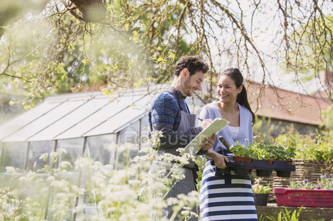 Работники питомников с планшетом и горшечными растениями в солнечном саду — стоковое фото