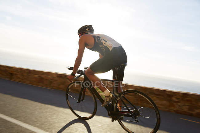 Male triathlete cyclist cycling on sunny ocean road — Stock Photo
