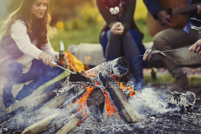 Friends cooking hot dogs and drinking beer at campfire — Stock Photo
