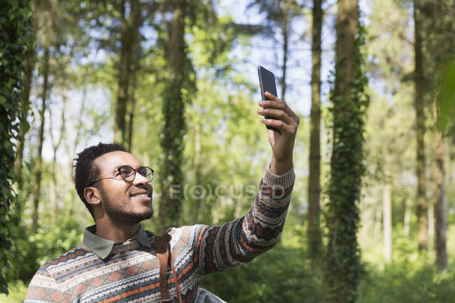 Улыбающийся мужчина делает селфи с фотоаппаратом в солнечном лесу — стоковое фото