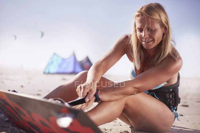 Femme fixation kiteboard aux pieds sur la plage ensoleillée — Photo de stock