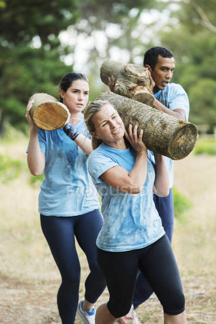 Determined woman running with log on boot camp obstacle course — Stock Photo