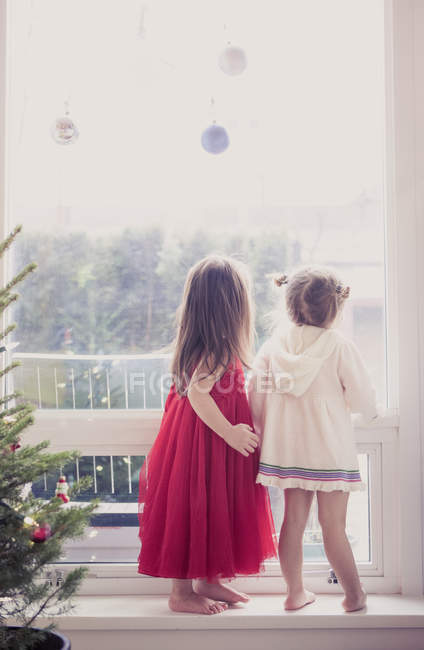 Girls on window ledge below Christmas ornaments — Stock Photo
