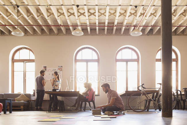 Kreativer Geschäftsmann auf Skateboard arbeitet am Laptop auf dem Boden im offenen Büro — Stockfoto