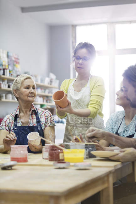 Enseignant guidant des étudiants matures peignant des poteries en studio — Photo de stock