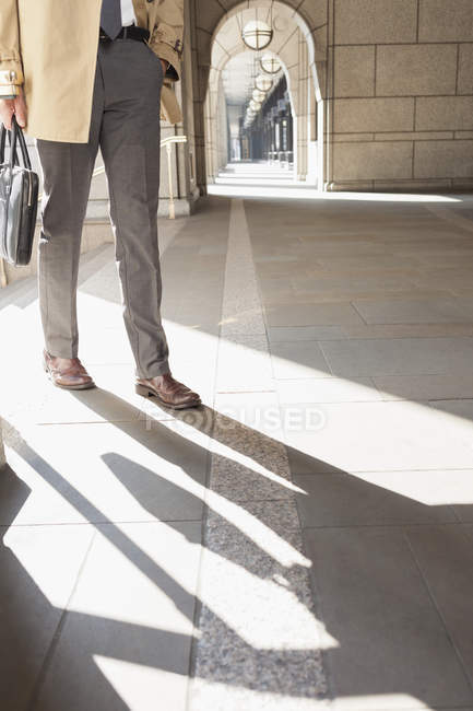 Empresário corporativo caminhando em claustro ensolarado — Fotografia de Stock