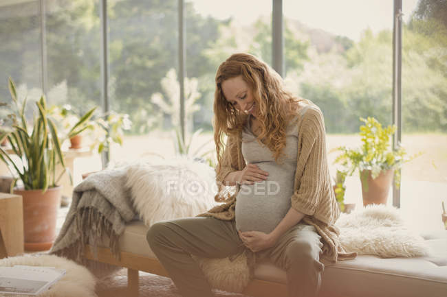 Sorridente donna incinta che tiene lo stomaco — Foto stock
