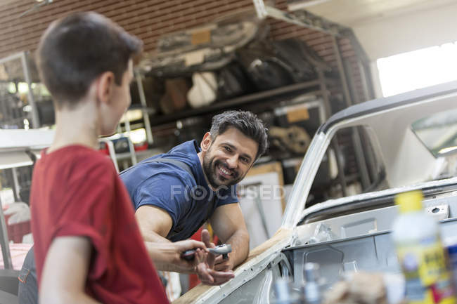 Улыбающийся отец забирает инструмент у сына в автомастерской — стоковое фото