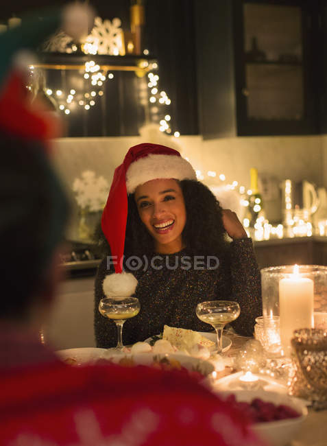 Mulher sorridente usando chapéu de Papai Noel no jantar de Natal à luz de velas — Fotografia de Stock