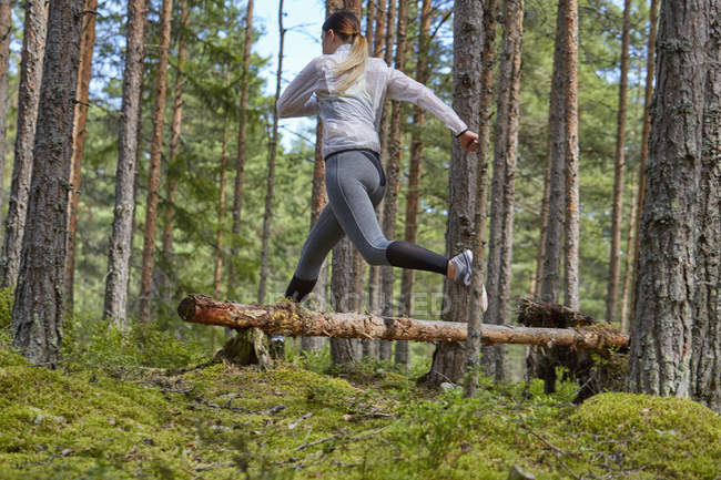Runner jumping over fallen log in woods — Stock Photo