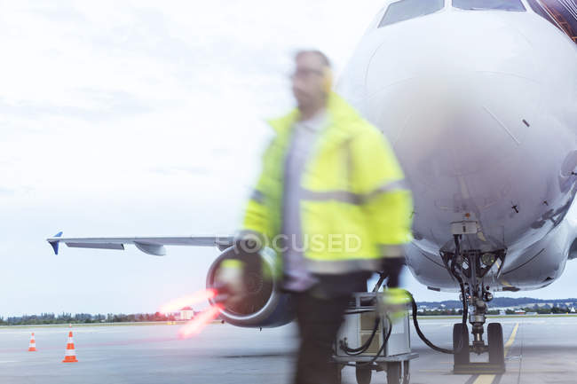 Controlador de tráfico aéreo caminando más allá del avión en asfalto - foto de stock