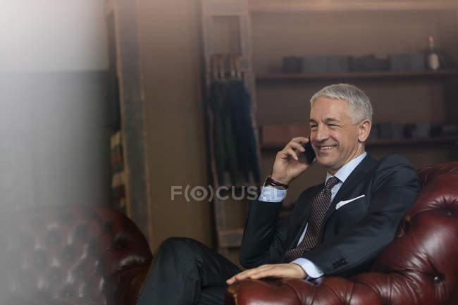 Homem de negócios sorrindo falando no celular na loja de moda masculina — Fotografia de Stock