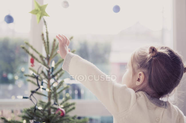 Girl reaching for start on Christmas tree — Stock Photo