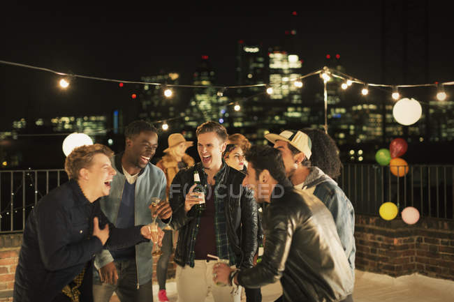 Young men drinking and laughing at rooftop party — Stock Photo