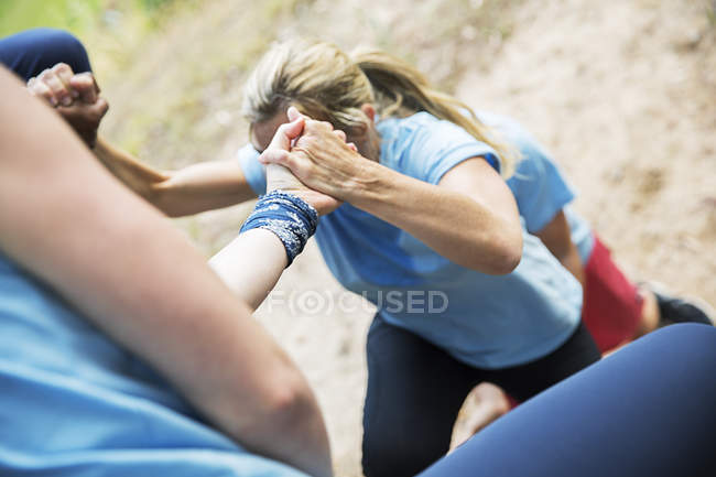 Teammates helping woman climb boot camp obstacle course — Stock Photo