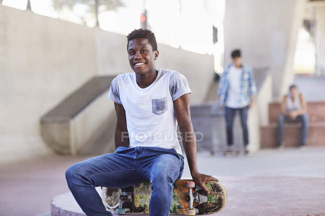 Portrait smiling teenage boy sitting on skateboard at skate park — Stock Photo