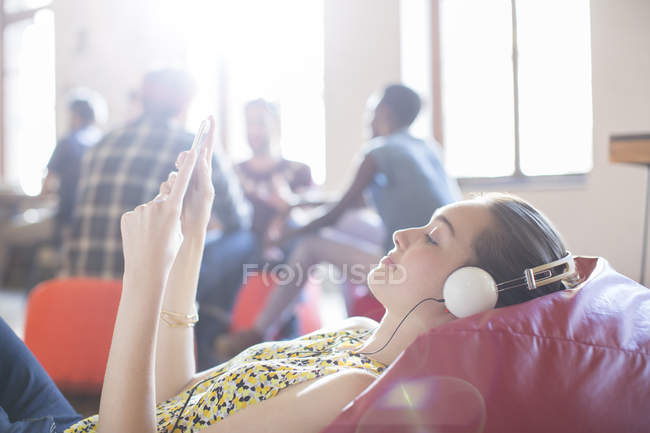 Donna d'affari casual rilassante con cuffie e tablet digitale sulla sedia sacchetto di fagioli — Foto stock
