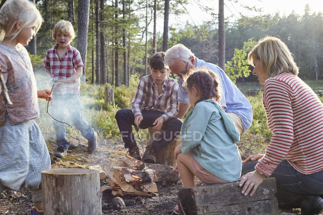 Abuelos y nietos disfrutando de una fogata en el lago - foto de stock