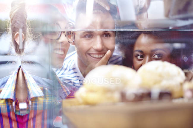 Friends pointing at desserts in display case at cafe — Stock Photo