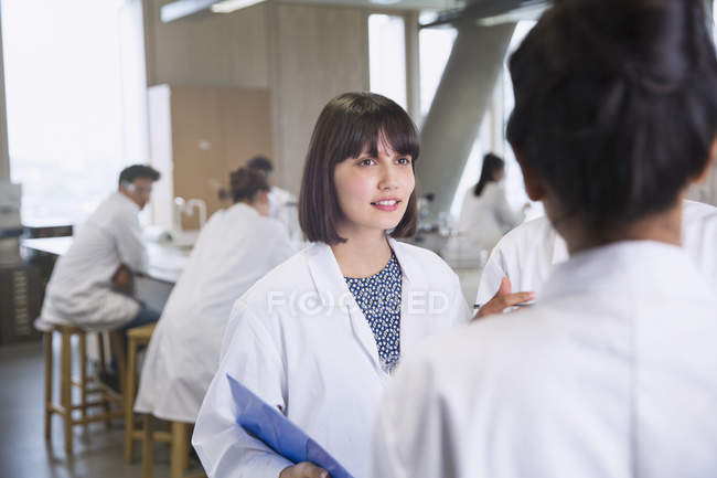 Studenti universitari di sesso femminile in camici a parlare in aula laboratorio di scienze — Foto stock