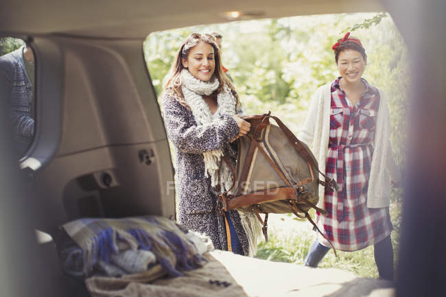 Smiling woman loading backpack into back of car — Stock Photo