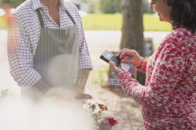 Planta vivero trabajador esperando como mujer utiliza máquina de tarjeta de crédito - foto de stock