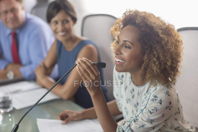 Bella donna seduta al tavolo da conferenza a parlare in microfono — Foto stock