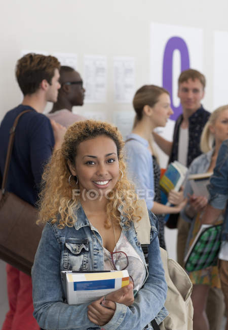 Estudiante sosteniendo libros y sonriendo a la cámara con un grupo de estudiantes en segundo plano - foto de stock