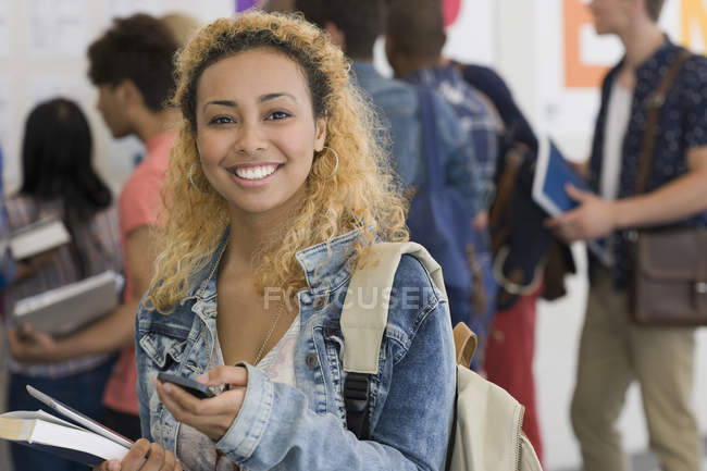 Estudiante sonriente usando el teléfono celular con otros estudiantes en segundo plano - foto de stock