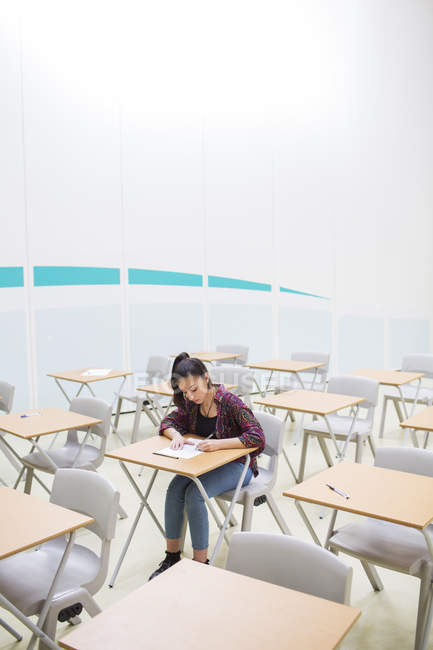 Estudiante sentada sola en el aula durante el examen GCSE - foto de stock