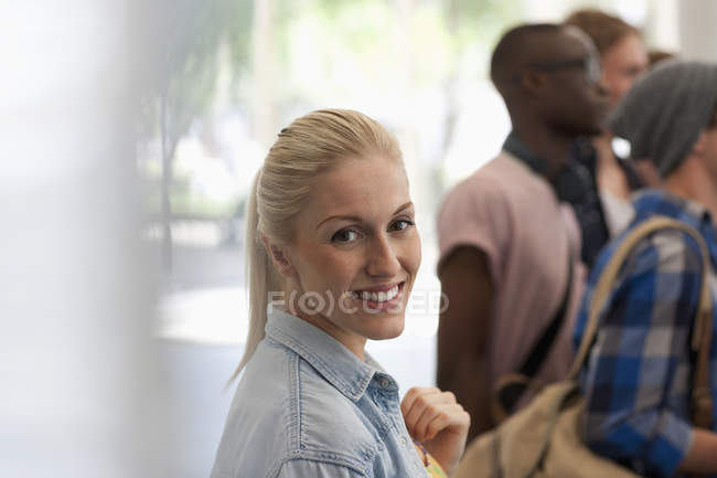 Sorridente studentessa guardando la macchina fotografica con altri studenti in background — Foto stock