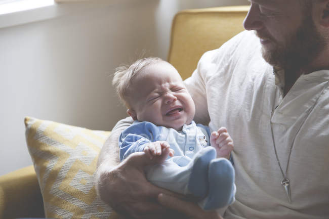 Padre sosteniendo y mirando llorando bebé - foto de stock