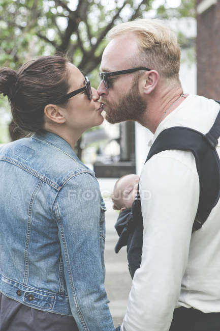 Вид пари в сонцезахисних окулярах цілує і тримає дитину на міських вулицях — стокове фото
