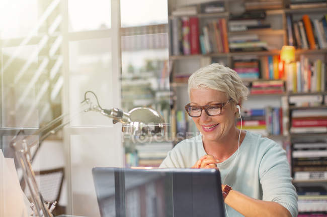 Businesswoman listening to earbuds and working in home office — Stock Photo