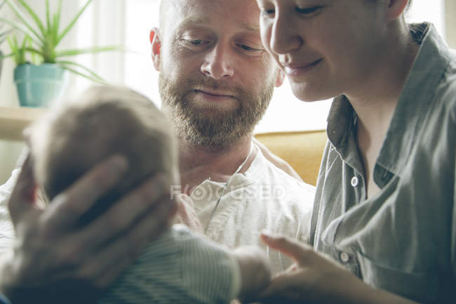 Vista de los padres sonriendo y sosteniendo al pequeño bebé - foto de stock
