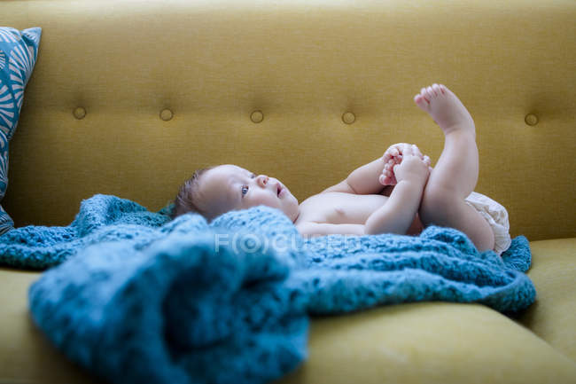 Pequeño bebé acostado sobre tela azul con las piernas levantadas, sosteniendo un pie - foto de stock